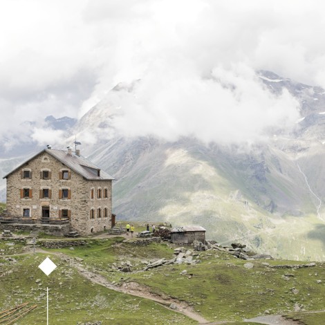 Rifugio Coston: Protetta in una conca rocciosa e circondata da terreni erbosi verde brillante. Il rifugio Coston in mezzo a un mare di nuvole.