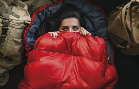 Rifugio Coston: Camere accoglienti con letti a castello e dormitori per un'esperienza autentica in baita. Una donna avvolta in un caldo e accogliente sacco a pelo da rifugio.